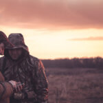 Two hunters in field looking at phone